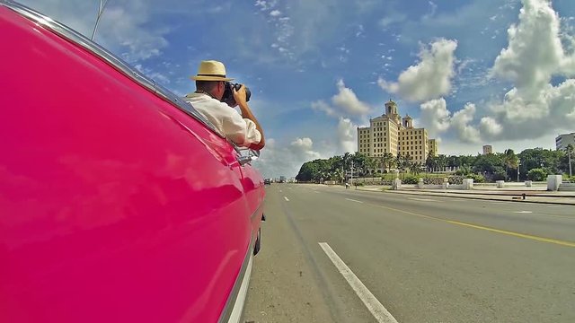 Drive through Havana city, man photographing from convertible car the city building