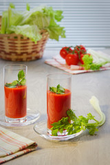 Two glasses with tomato juice, tomatoes, stalks and leaves of a celery on  table