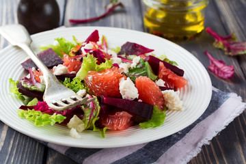 Salad of beets, lettuce, beetroot leaves, grapefruit and feta cheese on the old wooden background. Selective focus.