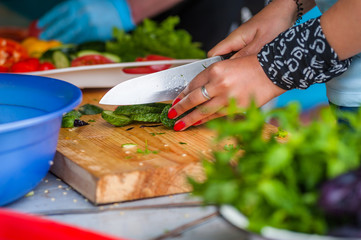 Women's hands cut fresh vegetables.