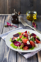 Salad of beets, lettuce, beetroot leaves, grapefruit and feta cheese on the old wooden background. Selective focus.