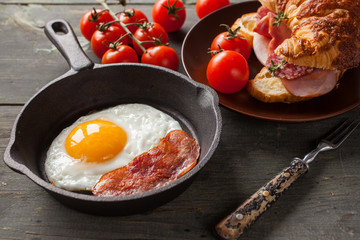 fried eggs with bacon and croissant with sausage on an old wooden background, selective focus