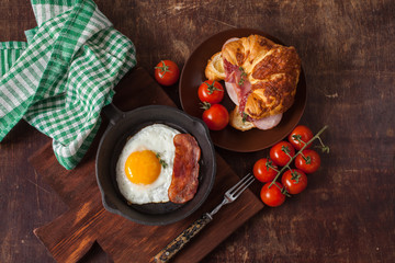 fried eggs with bacon and croissant with sausage on an old wooden background, selective focus