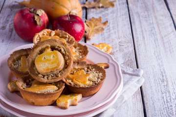 Delicious Tartlets mini tarts pie with pumpkin and apple for Halloween in a pink plate on wooden background