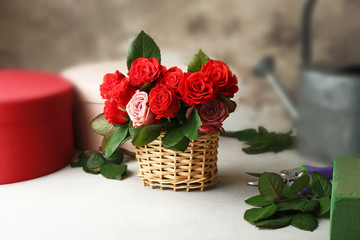 Wicker basket with beautiful bouquet of red roses on blurred background