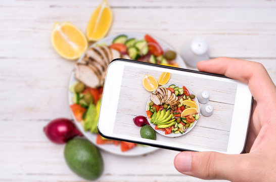 Hands taking photo mediterranean chicken salad with avocado with smartphone.