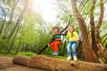 Happy kids jumping over a log in the summer forest