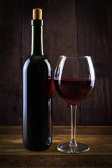 Bottle of red wine with glass. On a wooden table. On a black background.