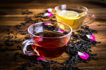 A cup of black and green tea with lemon. Tea leaves with rose petals. On a wooden background.