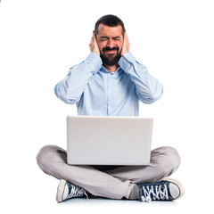 Man with laptop covering his ears