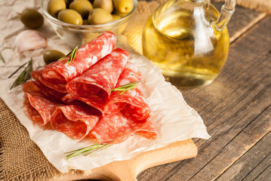 Italian salami with olives and spices on wooden background