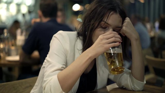 Drunk, sad woman drinking beer while sitting in the bar, 4K 
