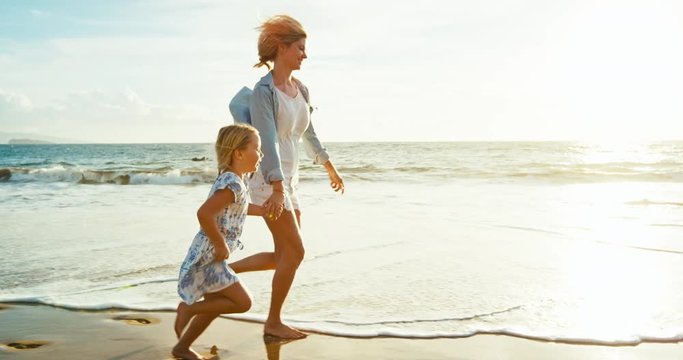 Mother and daughter having fun walking and playing on the beach at sunset - Powered by Adobe