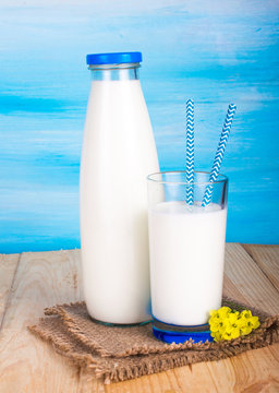 A bottle of milk, a glass of milk with straws. On a blue background.