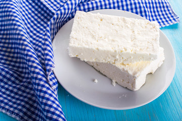 White cheese in the the saucer with a napkin. On blue, wooden background.