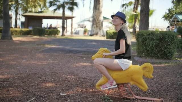 Young beautiful woman ride toy horse in a park playground