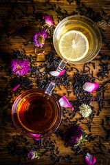 A cup of black and green tea with lemon. Tea leaves with rose petals. On a wooden background.