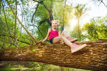 Cute girl sitting on fallen tree trunk in forest