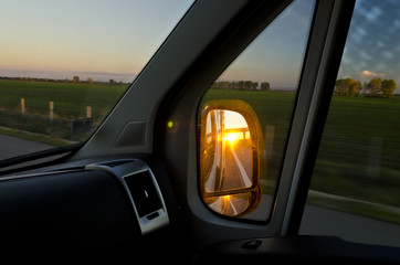Side rear-view mirror in the evening on the road during sunset