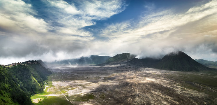 Amazing panorama view of mount Bromo with active volcano and village under cloudy sky. Java island landscape, Indonesia