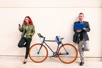 Woman and business man using mobile phone and pc leaning on white wall background with bike 