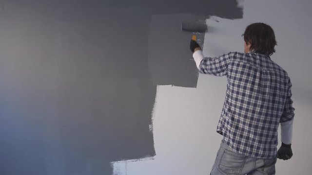 Male painter and interior decorator painting wall with gray color using paint roller