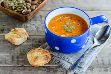 Pumpkin and carrot soup with nuts and bread buns on rustic wooden background