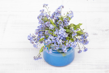 small blue flowers in a jar on a white wooden background