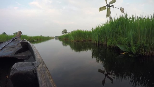 Wooden boat gliding through green reeds.