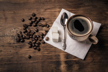 Cup of coffee with a spoon on a napkin and coffee beans