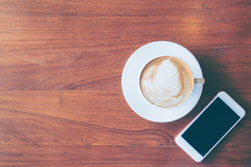 Top view of a cup of hot coffee and smartphone put on old wooden table background
