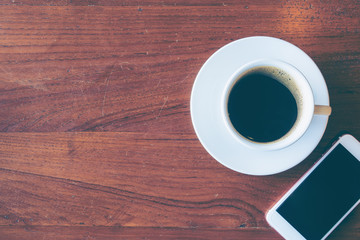 Top view of a cup of hot coffee and smartphone put on old wooden table background