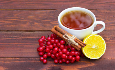 Healthy herbal tea with cinnamon, lemon and viburnum. White cup of hot tea with spices and berries on a wooden table.