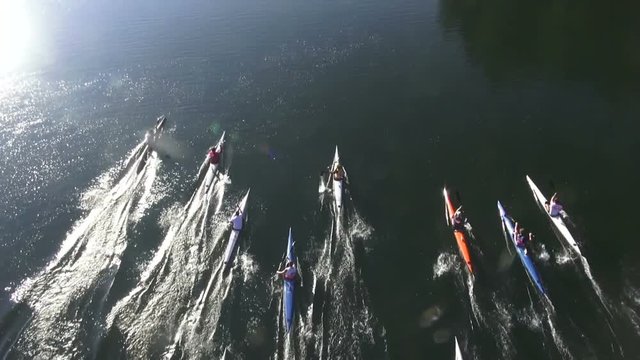 Team of rowing people in kayaks against camera in sunset