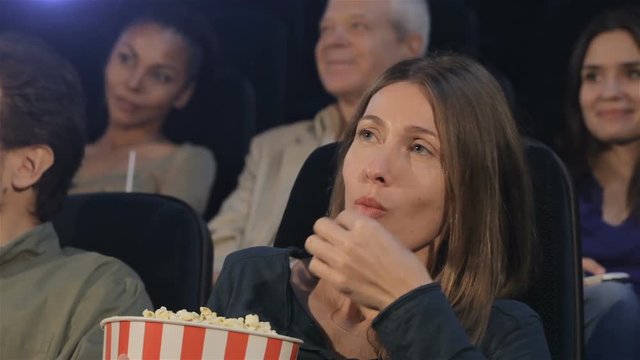 Woman puts popcorn into her mouth at the movie theater