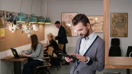 young handsome bearded man uses touchscreen tablet in the modern startup office.