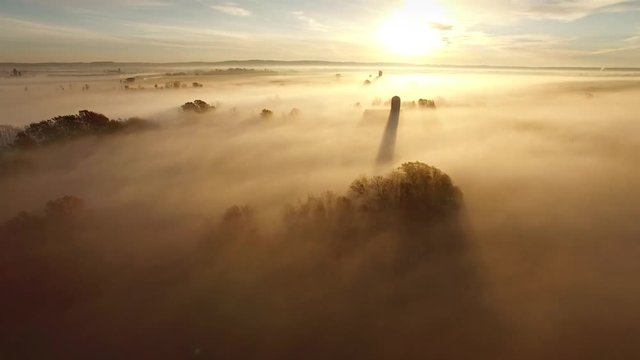 Foggy,breathtaking sunrise landscape with long shadow of silo, aerial view.
