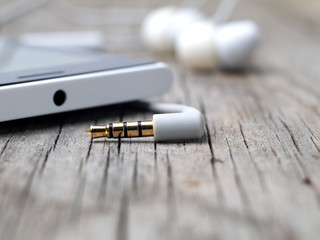 closeup of unplugged earphones mini-jack smartphone connector on wooden board, macro, shallow depth of field