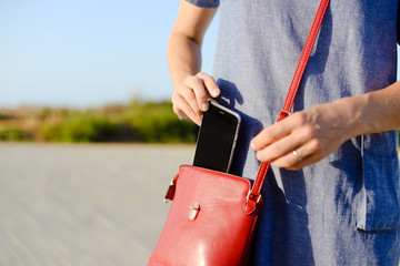 Closeup photo of stylish female taking cellphone out of handbag, sunny outdoors background - obrazy, fototapety, plakaty