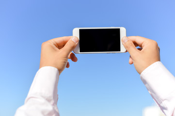 Closeup on mobile phone in the hand with blue sky on the background