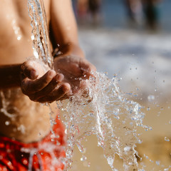 Fototapeta premium Hand and water, wet sand blurry outdoors background, close up image