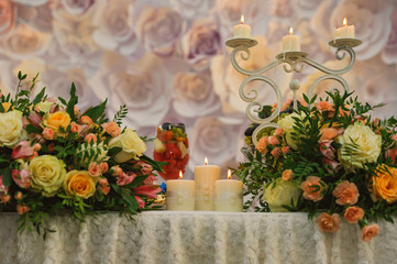 Burning candle standing on table in environment of flowers