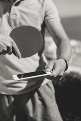 Black and white closeup on person hand using smartphone with black screen and ping-pong racket