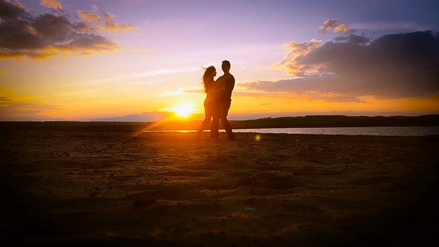 enamored guy and the girl on the beach dancing, whirling, cuddling on the beach, sunset, against a background of blue sky and water