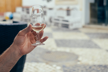Closeup on human hand holding wine glass, bar restaurant terrace on background