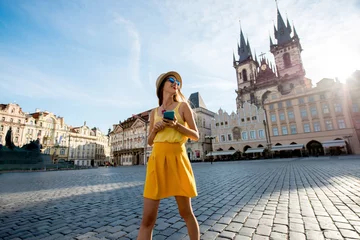 Fotobehang Praag Jonge vrouw in het geel wandelen met slimme telefoon op het oude stadsplein in de stad Praag