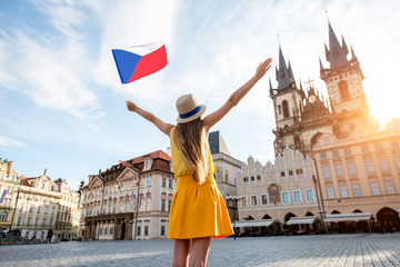 Fototapeta premium Młoda turystka kobieta ubrana na żółto, trzymając czeską flagę na rynku starego miasta w Pradze. Wspaniałe wakacje w Czechach