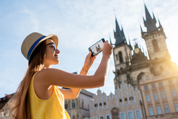Naklejka premium Young female tourist photographing with smart phone Tyn cathedral on the old square of Prague. Enjoying great vacation in Czech republic