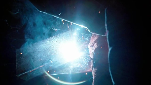 Welding a piece of metal in slow motion, sparks flying around, close shot showing mask, welding and smoke.