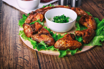 delicious grilled chicken wings with garlic and tomato sauce with lettuce on a round board on wooden rustic background